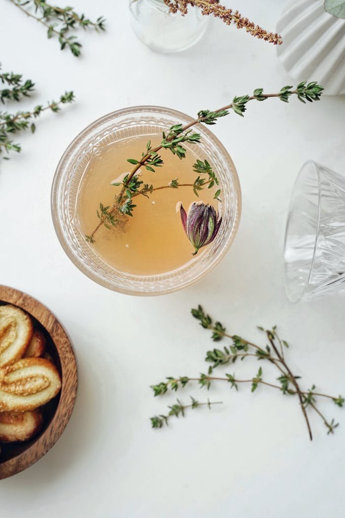 Elegant flatlay of herbal tea garnished with thyme and served with cookies, captured from above.